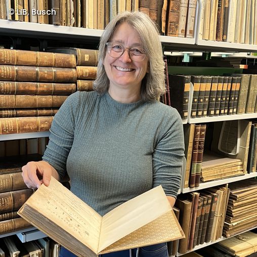 Katharina Schmidt-Loske mit einem alten Buch in der Hand vor einem Bücherregal mit historischen Büchern und Dokumenten